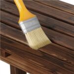 A brush is being used to paint a wooden bench.