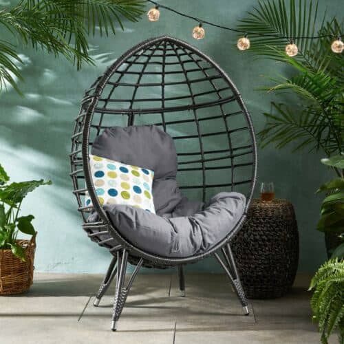 A black rattan chair with a cushion in front of plants.