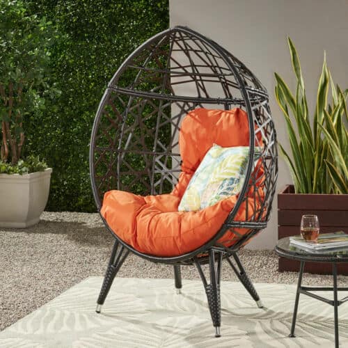 A black rattan chair with an orange cushion.