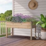 A wooden planter box with purple flowers and plants on a porch.