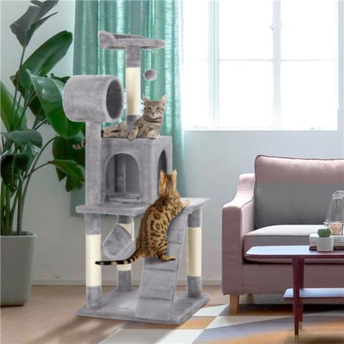 Two cats playing on a scratching tower in a living room.