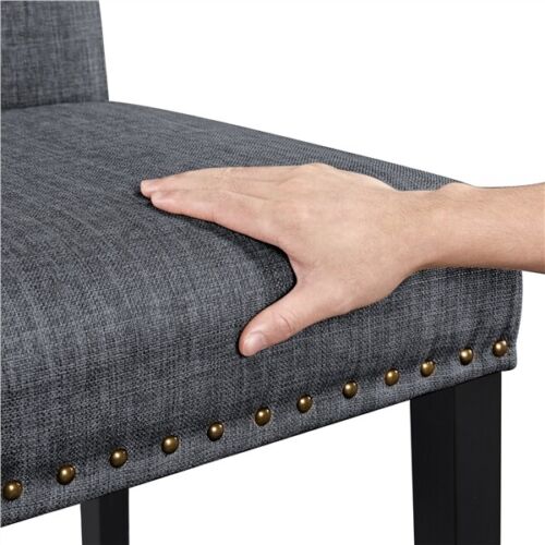 A hand is touching a gray upholstered chair with studs.