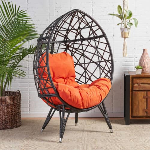 Black rattan egg chair with orange cushion.