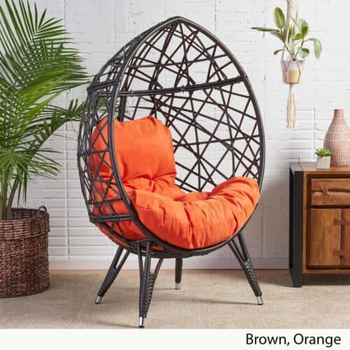 A rattan egg chair with orange cushion in front of a potted plant.