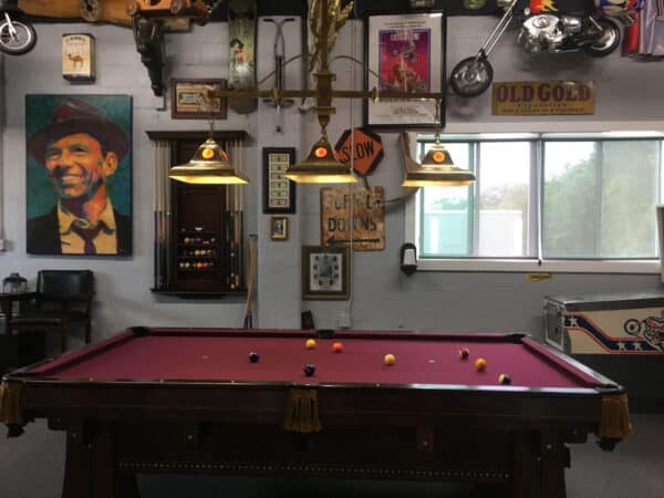 A pool table with balls set up for a game in a vintage-styled room with eclectic wall decor and hanging lights.