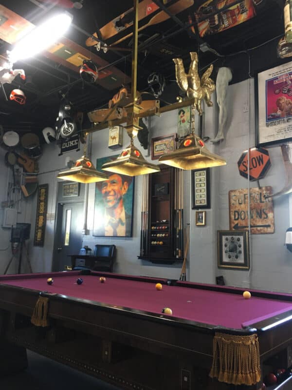A pool table with a magenta felt surface in a room decorated with eclectic memorabilia and overhead lighting.