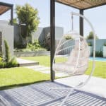 A white hanging chair in a backyard with a pool.