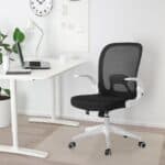 A modern home office setup with a black swivel chair, white desk, laptop, plant, and wall clock.