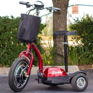 Three-wheeled electric mobility scooter parked outdoors with a storage basket attached to the handlebars.