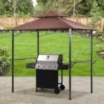 A gas grill under a patio gazebo in a backyard garden setting.