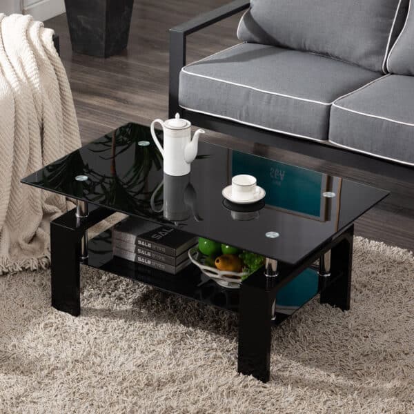 A modern black coffee table with a glass top in a living room, adorned with books, a fruit bowl, and a coffee set.