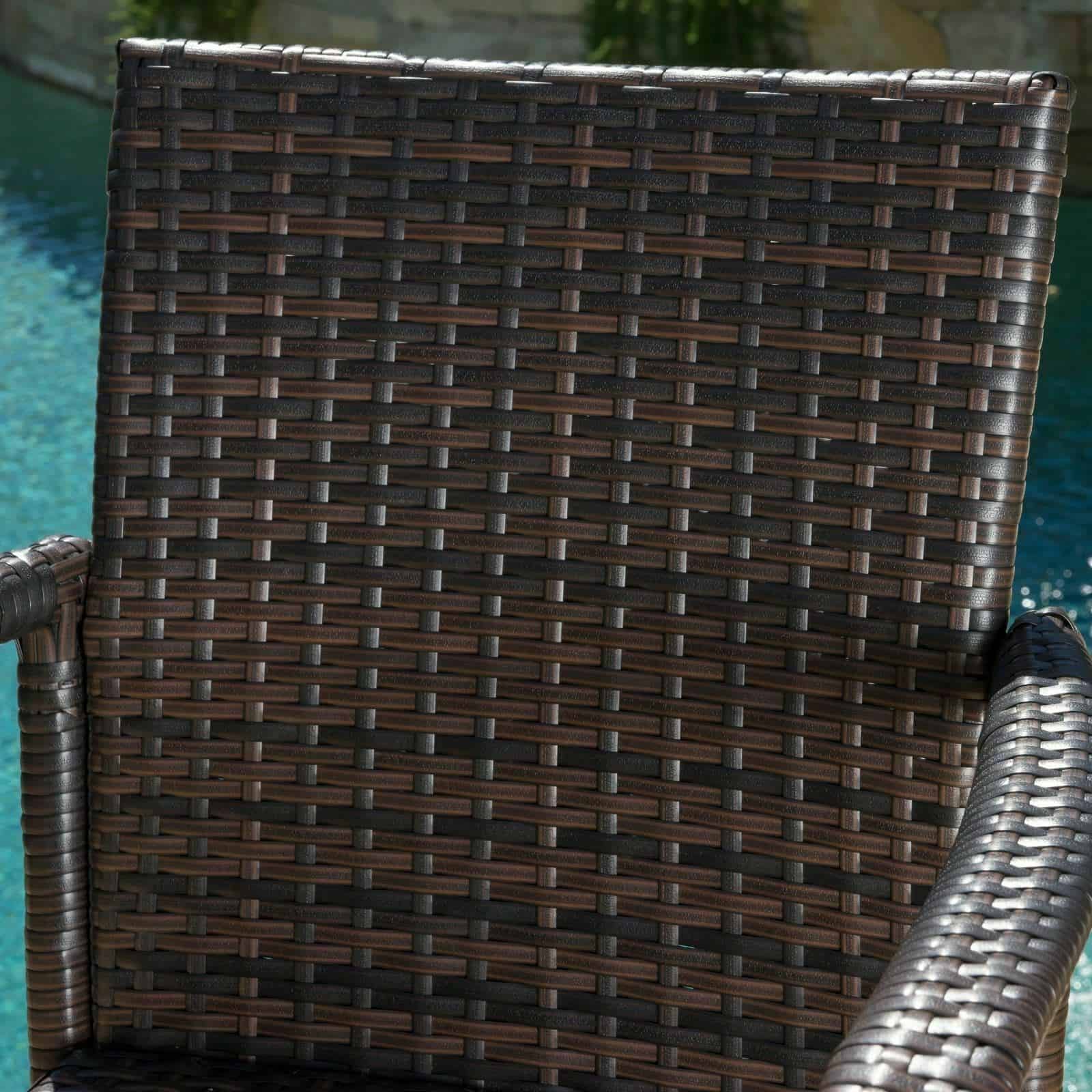 A wicker dining chair in front of a pool.
