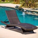 A wicker chaise lounge in front of a pool.