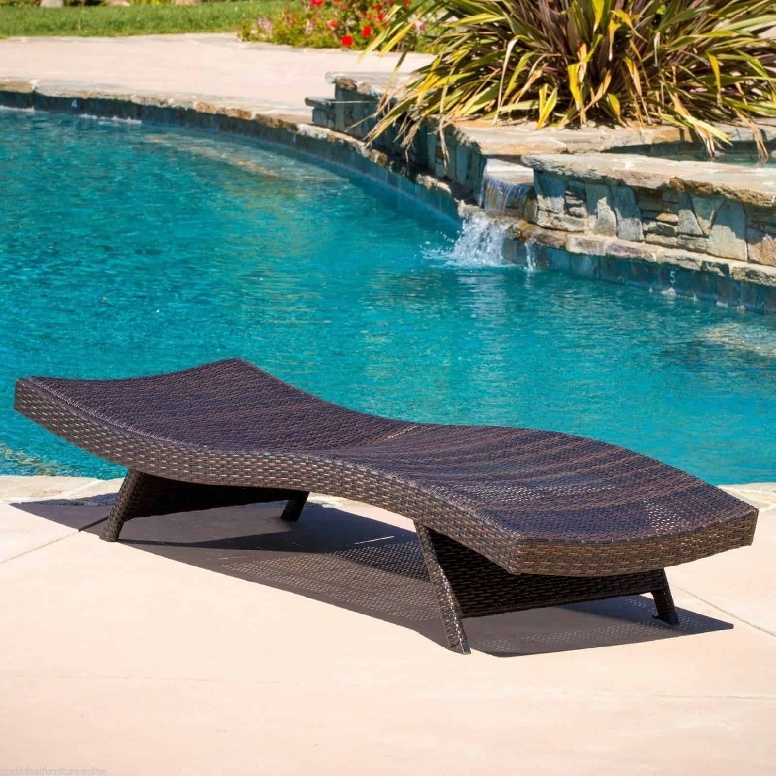 A wicker chaise lounge in front of a pool.
