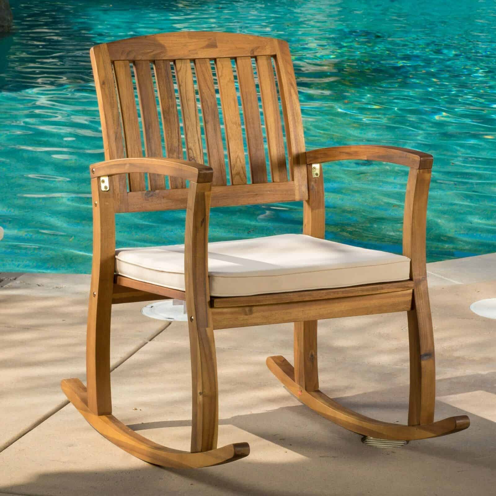 A wooden rocking chair in front of a pool.