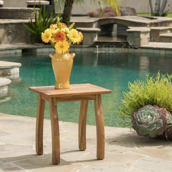 A teak side table in front of a pool.