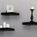 Three black shelves with candles and vases on them.