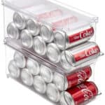 Two cans of coca cola in a clear storage container.