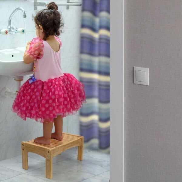 A little girl standing on a stool in a bathroom.