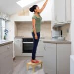 A woman standing on a stool in a kitchen.