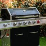 A black grill with four burners in the grass.