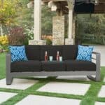 A black sofa with blue pillows on a patio.