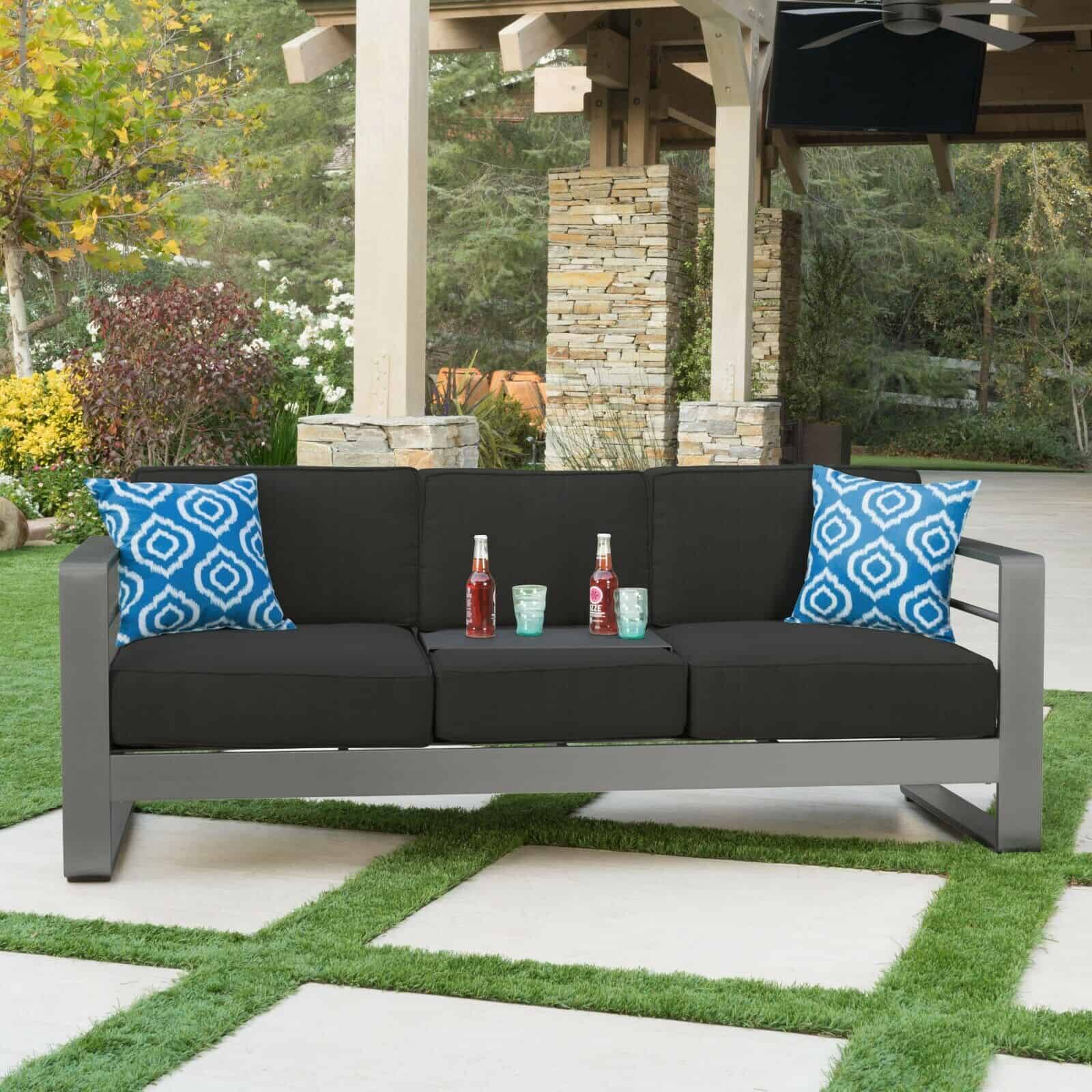 A black sofa with blue pillows on a patio.