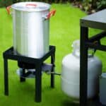 A large pot on a stand next to a propane tank.