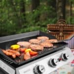 A barbecue grill with burgers and vegetables on a picnic table.