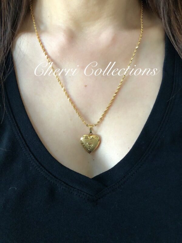 A woman wearing a gold necklace with a heart shaped locket.