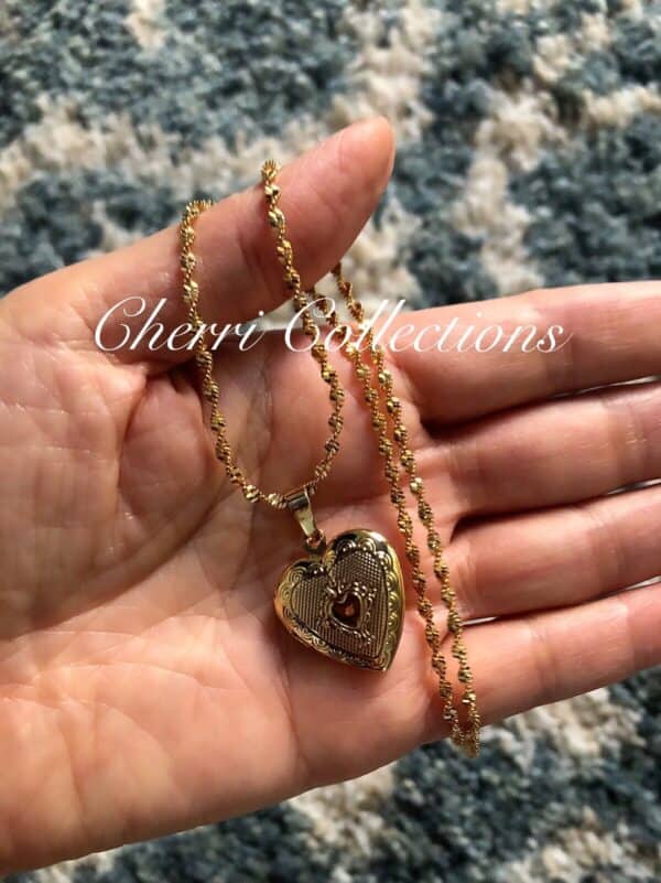 A hand holding a gold heart locket necklace.