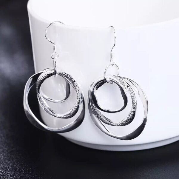 A pair of silver dangling earrings on top of a cup.