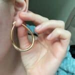 A woman putting on a pair of gold hoop earrings.