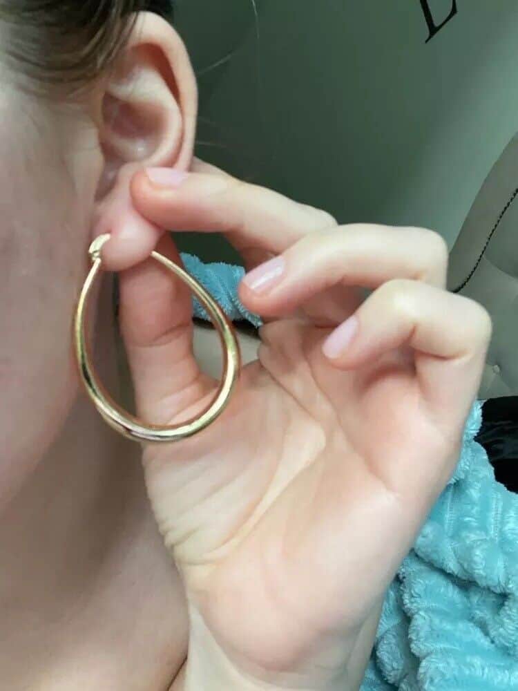 A woman putting on a pair of gold hoop earrings.