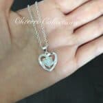 A woman's hand holding a silver heart necklace.