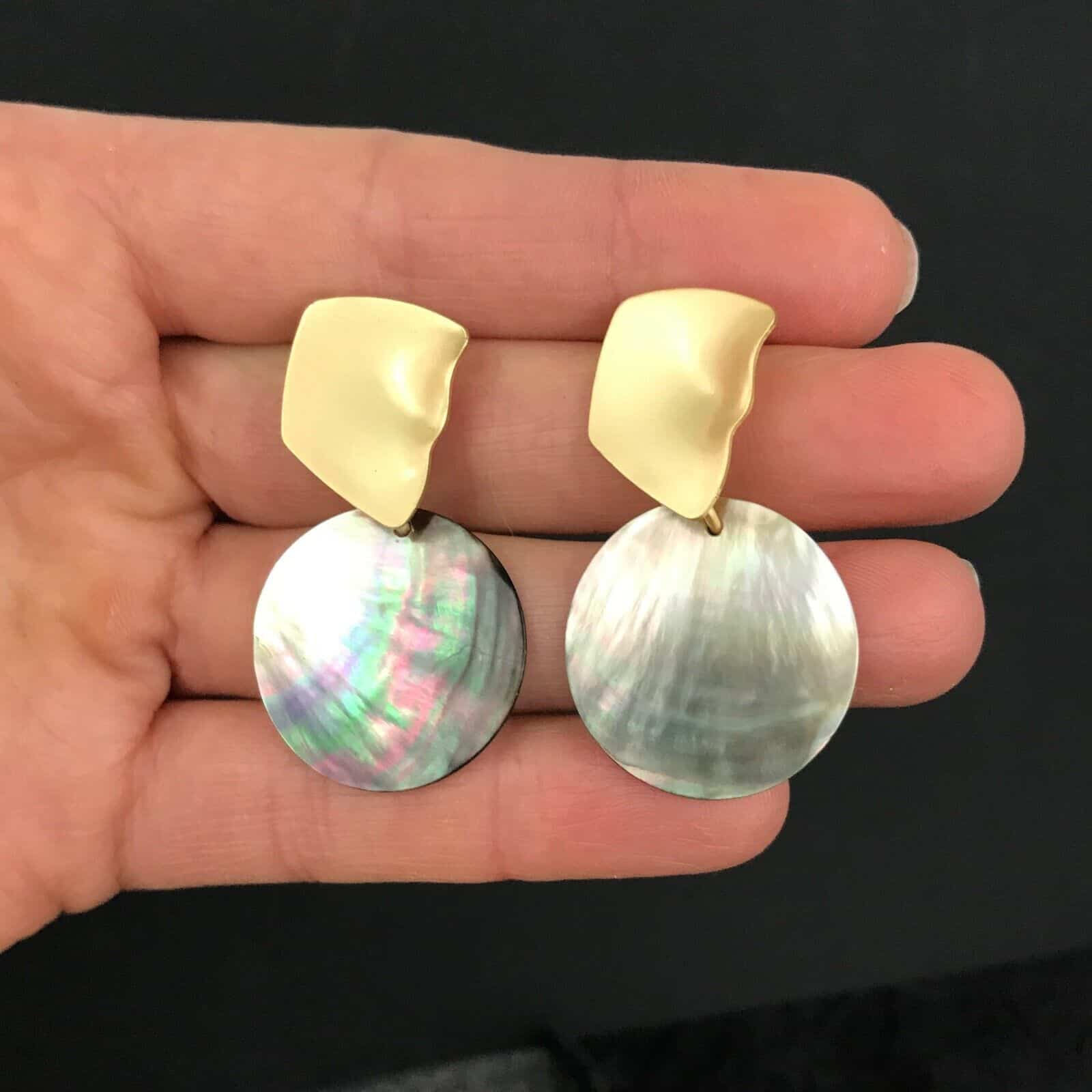 A pair of mother of pearl earrings in a hand.