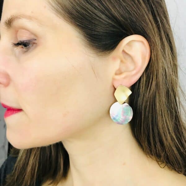 A woman wearing a pair of earrings with a gold disc.