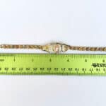 A gold bracelet with a ruler next to it.