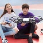 Two people sitting on the ground playing with a drone.