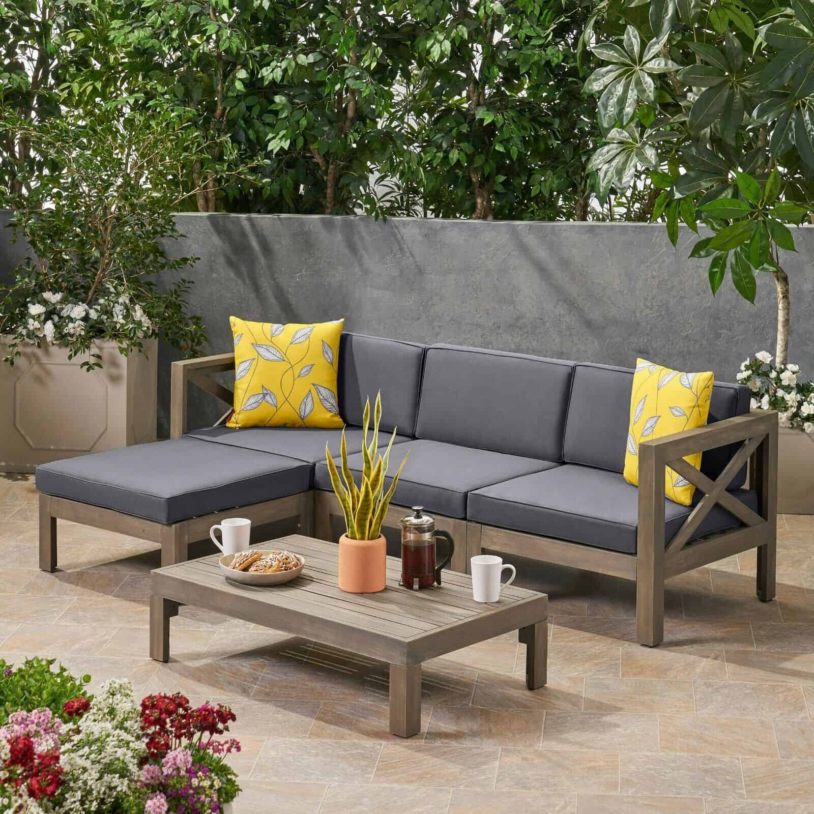 A grey sectional sofa set with yellow pillows on a patio.