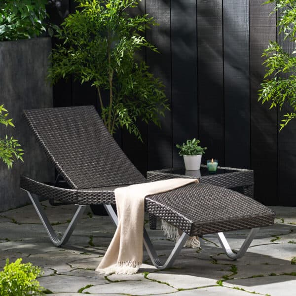 A black wicker chaise lounge in a garden.