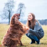 A woman kneeling on grass with a dog.