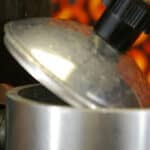 Close-up of a pot lid slightly ajar with steam escaping, against a blurred orange background.