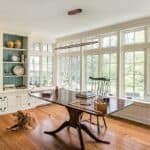 A spacious, well-lit home office with large windows, a traditional desk, and a 39"Wood Linear Pendant Light LED Dimmable Hanging Light Fixture Wood Linear Light Island Lights 24w Walnut illuminating the space where a golden retriever lies on the floor.