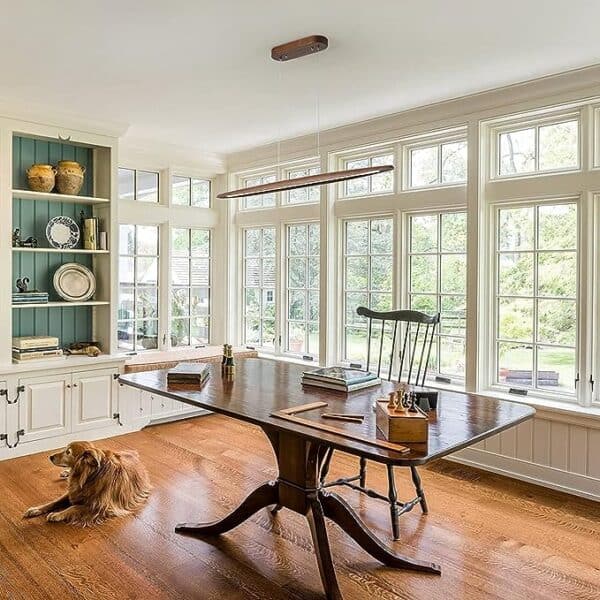 A spacious, well-lit home office with large windows, a traditional desk, and a 39"Wood Linear Pendant Light LED Dimmable Hanging Light Fixture Wood Linear Light Island Lights 24w Walnut illuminating the space where a golden retriever lies on the floor.
