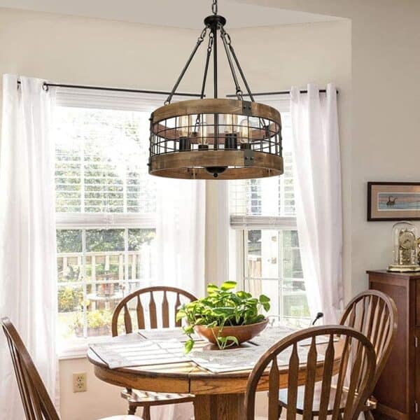 Contemporary dining room featuring a round wooden table with a plant centerpiece, wooden chairs, and a Farmhouse Rustic Chandelier Light Fixture 4-Light Round Hanging Pendant Lighting Black Wood and Black Metal Finish, with a view of a green garden through white-curtained windows.