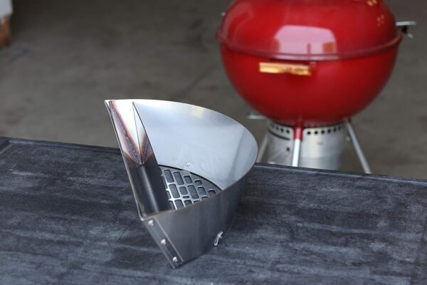 A Slow ‘N Sear® Deluxe for 22" Charcoal Grill on a black table, with a red charcoal grill in the background.