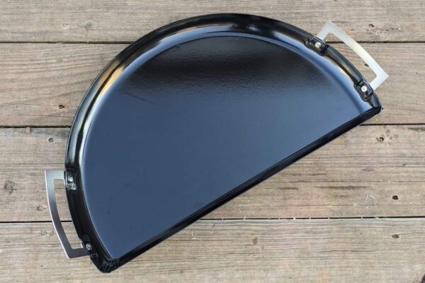 A black Slow 'N Sear Drip 'N Roast Porcelain Grill Pan with metal mounting brackets, resting on a wooden surface.