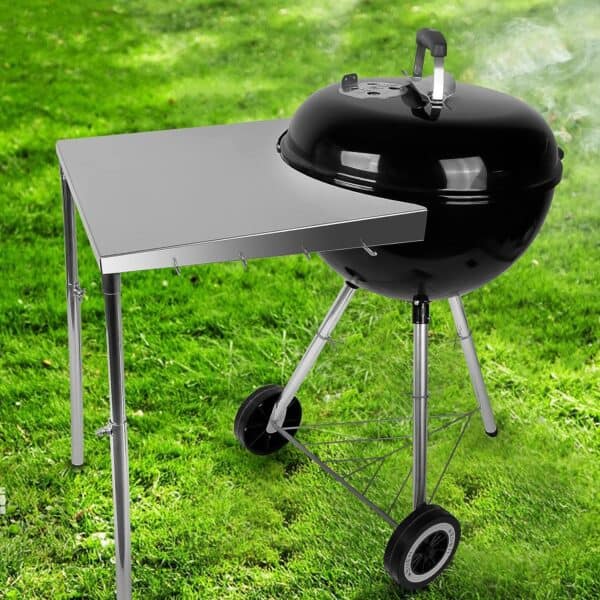 Stanbroil Stainless Steel Charcoal Grill with a Side Table on Wheels, smoking slightly, set on a green grass background.