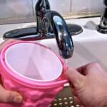 A person fills The Ultimate Mini Ice Cube Maker Pink Silicone Bucket Ice Mold and Storage Bin Portable 2 in 1 Ice Cube Maker with water from a kitchen sink faucet to use in The Ultimate Mini Ice Cube Maker.